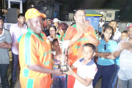 Young Richie Deonarain hands over the trophy to Erva Giddings of the Karibee Girls following their team’s defeat of Trophy Stall Angels last Sunday at Crabwood Creek.