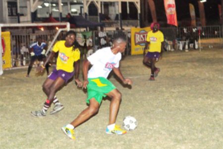 Eon Alleyne (white) of Festival City on the attack against Kitty Weavers during their group stage match in the Busta Football Championships
