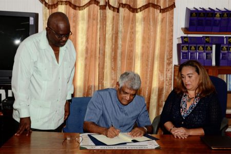 GECOM Chairman Dr Steve Surujbally signing the document in the presence of Lisa Shoman (right) and Chief Election Officer Keith Lowenfield. (GECOM photo)