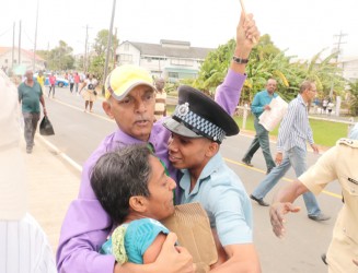 Ronald Bulkan attempting to rescue activist, Sherlina Nageer after a male police officer tried to stop her from protesting at the entrance of the Marriott Hotel.  