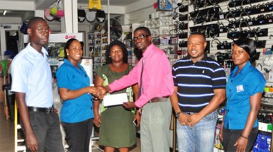 2Js General Store Supervisor Loyette Barnwell (2nd left) hands over the cheque to Petra Organization member Mark Alleyne (4th left) while other members of company and the Petra Organization inclusive of Co-Director Troy Mendonca (2nd right) look on   