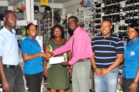 2Js General Store Supervisor Loyette Barnwell (2nd left) hands over the cheque to Petra Organization member Mark Alleyne (4th left) while other members of company and the Petra Organization inclusive of Co-Director Troy Mendonca (2nd right) look on
 
