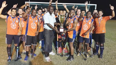 Devin Hooper receiving the championship trophy from Farfan & Mendes Limited Marketing Officer Delon Josiah while other teams celebrate. 