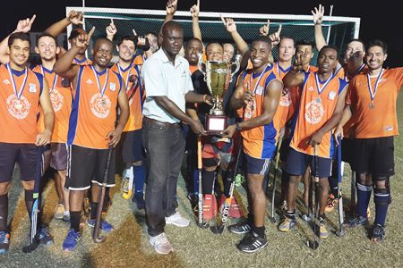 Devin Hooper receiving the championship trophy from Farfan & Mendes Limited Marketing Officer Delon Josiah while other teams celebrate.