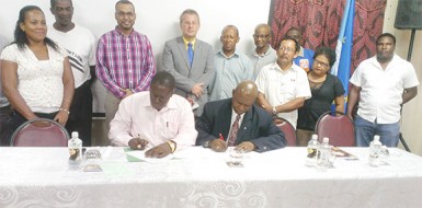 FAO Representative Reuben Robertson (right) signing the agreement for the pilot timber project with Manager of the Forestry Training Centre Inc Quancy Bremmer. Also in photo are: Natural Resources and Environment Minister Robert Persaud (third, left); Head of the European Delegation in Guyana, Ambassador Robert Kopecky (fourth, left) and some of the recipients of the project. 