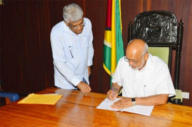 This Office of the President photo shows President  Donald Ramotar signing while Chairman of the  Guyana Elections Commission, Dr Steve Surujbally looks on. (GINA photo) 