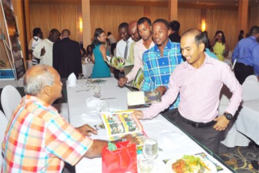 Guyana Jaguars players Vishaul Singh, Trevon Griffith and Paul Wintz line up to have their magazines signed by the icon