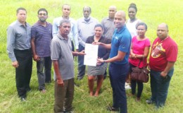 GFF Normalization Committee Chairman Clinton Urling (right) displaying the signed 30 year lease contract with the Eccles/Ramsberg Neighborhood Democratic Council (NDC) for the Providence Community Centre Ground while other members of the GFF Secretariat look on