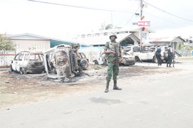 Sophia aftermath: A member of the Guyana Defence Force standing guard on Tuesday in front of the residence of Pastor Narine Khublall which was acting as a PPP/C command centre on Election Day in `C’ Field, Sophia. Monday’s unrest saw homes stoned and a small shack with a horse stable attached burnt. Eight vehicles (some in background) were also destroyed by arson after allegations that the command centre was operating an illegal polling station.