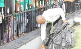 Law graduate Sherod Duncan taking on the responsibility of picking up garbage during the swearing in ceremony of APNU+AFC’s presidential candidate, David Granger yesterday at the Parliament Building. Persons in the crowd had thrown their empty plastic and beer bottles on the lawn.