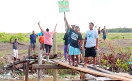 One would-be squatter holds aloft his marker as he along with others heads across a makeshift bridge at Success, East Coast Demerara yesterday afternoon to lay claim to land belonging to GuySuCo. (Photo by Arian Browne)
