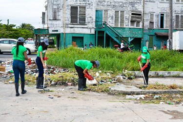 Gizmos and Gadgets staffers picking up garbage and raking the grass at the parking lot opposite the store.