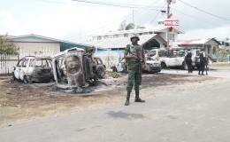 Sophia aftermath: A member of the Guyana Defence Force stands guard in front of the residence of Pastor Narine Khublall which was acting as a PPP/C command centre on Election Day in `C’ Field, Sophia. Monday’s unrest saw homes stoned and a small shack with a horse stable attached burnt. Eight  vehicles  (some in background) were also destroyed by arson after allegations that the command centre was operating an illegal polling station. 