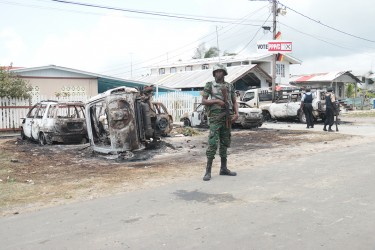Sophia aftermath: A member of the Guyana Defence Force stands guard in front of the residence of Pastor Narine Khublall which was acting as a PPP/C command centre on Election Day in `C’ Field, Sophia. Monday’s unrest saw homes stoned and a small shack with a horse stable attached burnt. Eight  vehicles  (some in background) were also destroyed by arson after allegations that the command centre was operating an illegal polling station. 