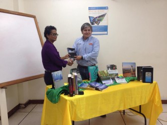  Dr Elizabeth Ramlal (left) shakes hands with Aurora gold project representative Marco Camacho as she receives the donated books. 