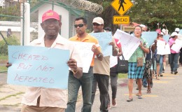 Former Local Government Minister Ganga Persaud bearing a placard outside GECOM, last month.
