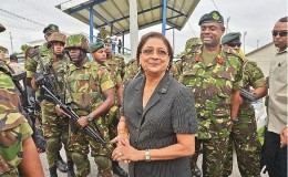 Heavy guard: Prime Minister Kamla Persad-Bissessar is surrounded by defence force troops during a visit on Saturday to Crown Trace, Enterprise, where an apparent gang war has erupted in the past few weeks. 