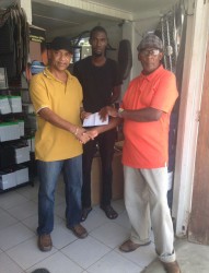 Mark Lewis of Lewis and Sons General Store at Rose Hall Town presents the cheque to race coordinator Randolph Roberts at the Lewis and Sons Store at Rose Hall while Neil Lewis looks on. 