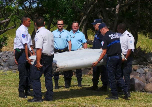 French gendarmes and police carry a large piece of plane debris which was found on the beach in Saint-Andre, on the French Indian Ocean island of La Reunion, July 29, 2015. Reuters/Zinfos974/Prisca Bigot