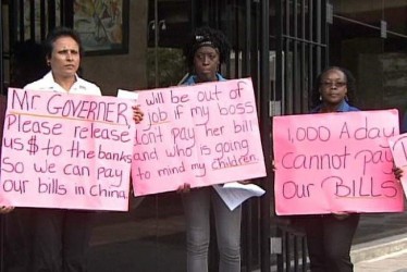 Businesswoman Mary Ramlogan, left, is joined by two of her employees as they hold up placards yesterday during their protest over the inadequate supply of foreign currency outside the Central Bank in Port of Spain. —Photo courtesy TV6