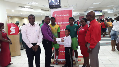 Young Romeo Deonarain receives the sponsorship check from Scotia Bank Business Manager Richard Damon in the presence of his teammates, club President Alfred Mentore and the bank’s executives Karen Harris and Brian Hackett. 