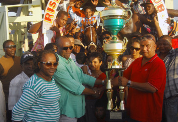 Handlers of Just Call Me Boss accepting the large winner’s trophy compliments of the Trophy Stall of Bourda Market. (Orlando Charles photo) 