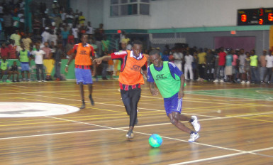 Okeene Fraser (orange) of Bent Street is in hot pursuit of Sparta Boss’s Travis Grant (green) during the final minutes of their tense GT Beer Futsal Championship finale at the Cliff Anderson Sports Hall