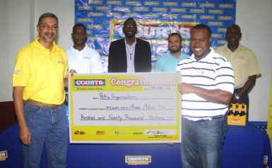 Petra Co-Director Troy Mendonca is all smiles as he receives the sponsorship cheque to the sum of 3.6 million dollars from Courts Guyana Incorporated CEO Clyde De Hass (right) during the launch of the 4th Annual Courts Pee Wee Football Tournament while other members of the launch team look on inclusive of Director of Sports Christoper Jones (centre) and Banks DIH Limited Malta Supreme Brand Manager Clayton McKenzie (right) 