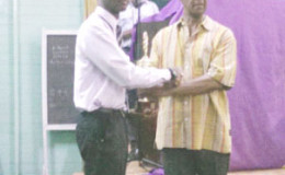 Republic Bank’s Davion Mars (left), who placed second in the Junior category of the Forbes Burnham Memorial Chess Tournament, receives his trophy and medal from PNCR senior official Lance Carberry at an awards ceremony at Carifesta Sports Club. The junior category of the Burnham Memorial was won by Roberto Neto.