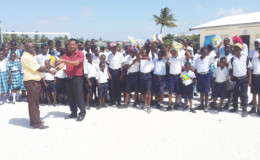 Guyana Volleyball Federation president John Flores hands over the equipment to Robin Phillips in the presence of the schoolchildren.