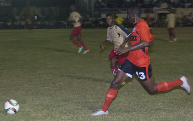 Jolanshoy McDowall (orange) of Slingerz FC in the process of making one of his trademark overlapping runs while being pursued by Kevin Cottoy of Monedderlust FC during their team’s showdown in the GFF Stag Beer Elite League at the GFC ground