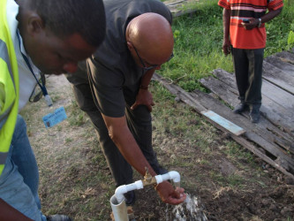 New GWI Chief Executive Officer (CEO) Dr. Richard Van West-Charles tests one of the standpipes that will be providing potable water to residents of Pattenson, North Sophia (GWI photo)