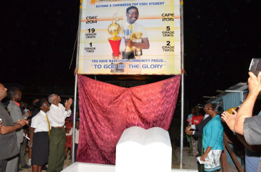 President David Granger (clapping) and 2014 CSEC top regional performer, Elisa Hamilton, who is also a 2015 top performer at CAPE,  unveiling a billboard in honour of her achievements, at the Ann’s Grove Market tarmac, last evening.   (Ministry of the Presidency photo) 