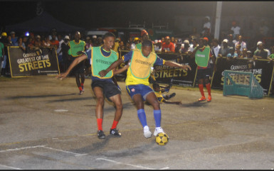 Hubert Pedro (yellow) of West Front Road trying to maintain possession of the ball while being challenged by a Castello Housing Scheme player during their team’s matchup in the Guinness of the Streets Georgetown Tourney at the California Square tarmac