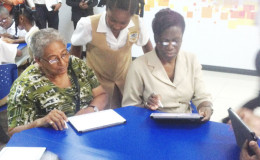 A student offers assistance to Ministry of Education Chief Planning Officer Evelyn Hamilton (left) and Permanent Secretary of the Ministry Delma Nedd as they test out the devices in the Smart Classroom.
