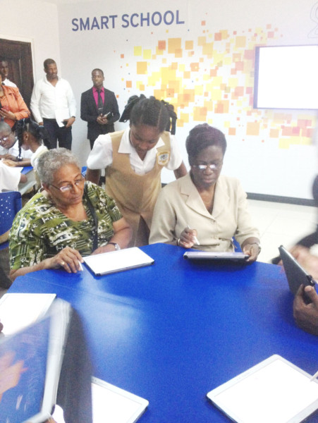 A student offers assistance to Ministry of Education Chief Planning Officer Evelyn Hamilton (left) and Permanent Secretary of the Ministry Delma Nedd as they test out the devices in the Smart Classroom.  
