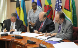 USAID’s Eastern and Southern Caribbean Mission Director Christopher Cushing (at left) and Caricom Secretary General Irwin LaRocque signing the aid agreement while US Ambassador Perry Holloway (centre) looks on. 