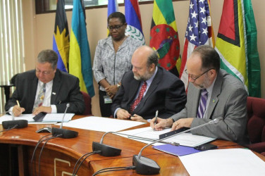 USAID’s Eastern and Southern Caribbean Mission Director Christopher Cushing (at left) and Caricom Secretary General Irwin LaRocque signing the aid agreement while US Ambassador Perry Holloway (centre) looks on. 