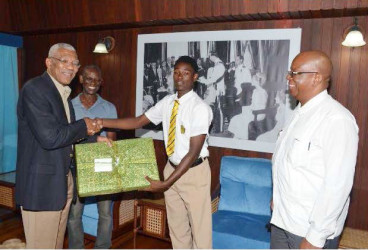 President David Granger presents Terron Alleyne with a new laptop computer, as Minister of Finance, Winston Jordan (right), and the lad’s father, Terrence Alleyne, looks on. (GINA photo) ​ 