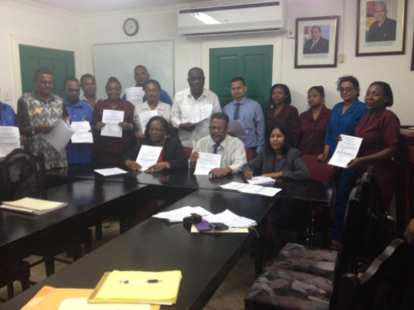 Chief Labour Officer Charles Ogle (seated at centre), CCWU representative Ann Anderson (seated at left) and DDL Director Moneeta Singh-Bird (seated at right) surrounded by trade unionists from the three unions as they all display their copies of the agreement.
