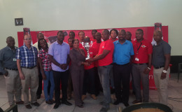 Banks DIH Limited captain Seon McKenzie collecting the championship trophy from the Ministry of Tourism PRO representative Marjorie Chester while other members of the team, the respective sponsors and the coordinating team looks on
 