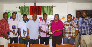 Captain of the victorious Milerock FC Joel McKinnon (centre) receiving the championship trophy from GTT PRO Allison Parker during the official Limacol/GTT Football Championship presentation ceremony while other members of his team, respective prize winners, sponsors and Petra Organization staff look on. 