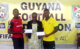 Alpha United’s Delon Lanferman (left) and Pele’s Jumane Somerset collecting their plane ticket from GFF Vice President Attorney-at-Law Thandi McAllister at the federation’s office prior to their departure for the MLS Combine in Curacao