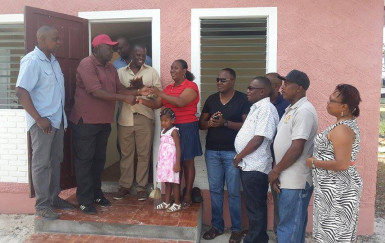 Natasha Dash receiving the keys to her newly renovated house yesterday from Eswick Northe of The Garage, while other members of the community who helped make it possible look on 