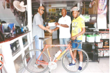 In picture Neal Lewis of the Lewisons’ store at Rose Hall Town presents a cheque of an undisclosed sum to organizer Randolph Roberts at  Rose Hall Town, Corentyne, Berbice  while young cyclist Zamar Khan displays his new bike.   