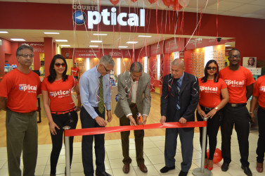 Managing Director of Courts Clyde de Haas is flanked by Minister of Business Dominic Gaskin and Minister of Public Health George Norton (at his right and left respectively) along with Courts staff as he cuts the ribbon for the opening of Courts Guyana’s optical department at its Main Street store.  