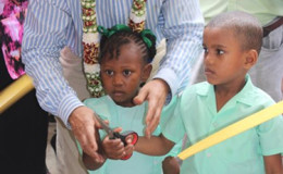 Minister of Education, Dr Rupert Roopnaraine with pupils of the Cummings Park Nursery at the symbolic cutting of the ribbon (Ministry of Education photo)
