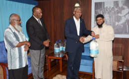 President David Granger (second from right) shares a warm handshake with Shaykh Abdul Aleem Rahim, President of the Guyana Islamic Trust, as he presents him with a bottle of Zamzam water, while Minister of State Joseph Harmon (second from left) and another representative look on, during a meeting today at the Ministry of the Presidency. (GINA photo)
