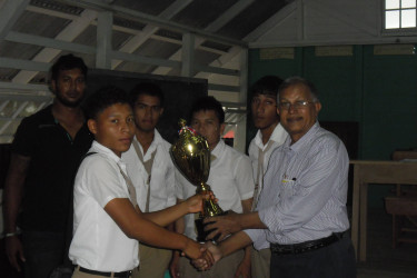 Forty students from 10 secondary schools and one primary school, contested the sixth Berbice Inter-School Chess Championship in November at the Manchester Secondary School. Skeldon Secondary emerged victorious in the event. Veral Felix of Orealla Secondary captured the second place prize in the individual category. A report of the Berbice competition indicated that Felix made the journey from his village of Orealla with his mother by boat, leaving at 11 o’clock on the night before the tournament. Darwin London of the Berbice Educational Institute won the first prize in the individual category. The competition was organized by Krishnanand Raghunandan, an official of the Guyana Chess Federation. In photo Raghunandan (right) presents a trophy to one of the winners.  
