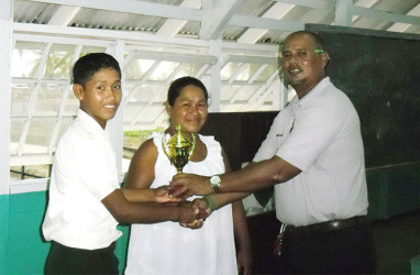 Student of the Orealla Secondary School, Veral Felix, 15, smiles as he is rewarded with a trophy for placing second in the individual category of the Sixth Berbice Inter-School Chess Championship held in November at the Manchester Secondary School. Presenting the trophy is Berbice High School teacher Zahir Moakan (right). Veral travelled to the chess competition from Orealla in the Berbice river with his mother, starting out at 11 o’clock at night by boat.
